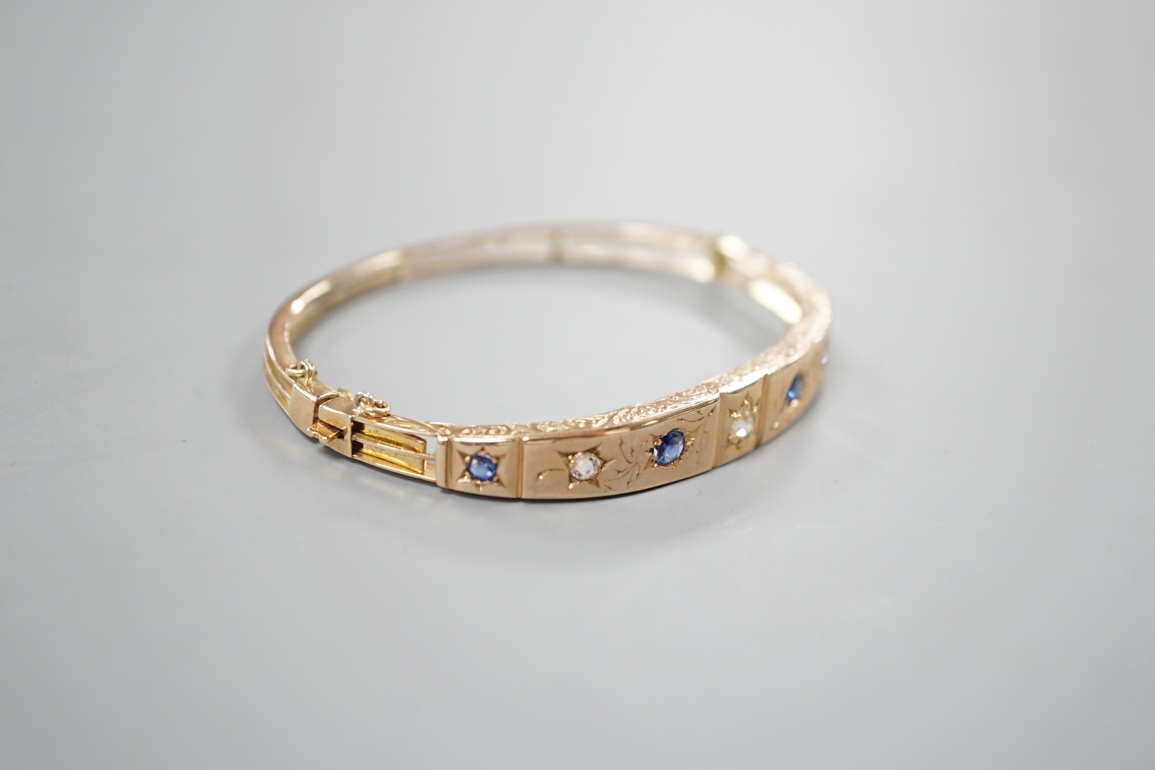 A late Victorian engraved yellow metal, four stone sapphire and three stone diamond set hinged bangle, gross 10.5 grams.